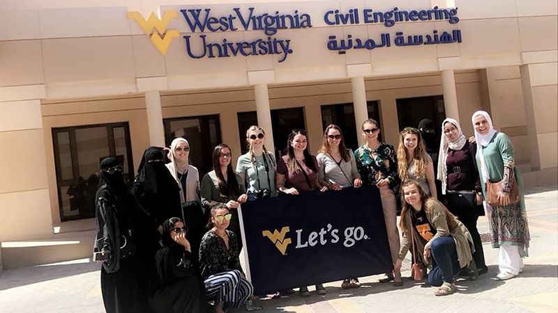 Group in front of WVU Civil Engineering building in Bahrain holding a flag that says "Let's go"