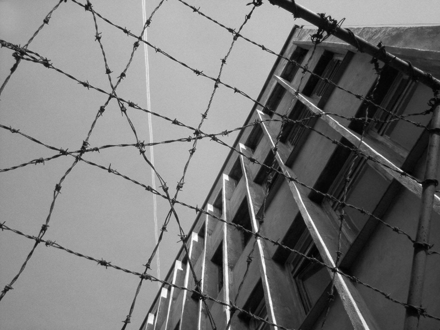 Barbed wire in the foreground, outside prison wall and sky in background