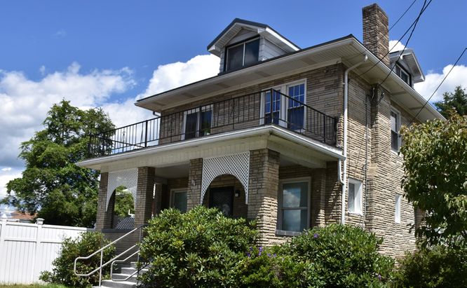 Three story home exterior, tan brick/stone, porch on bottom floor and balcony on second