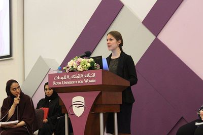 Clara speaking at a podium that reads "Royal University for Women"
