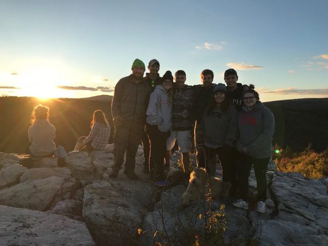 Group smiling standing on rocks with sunset in background