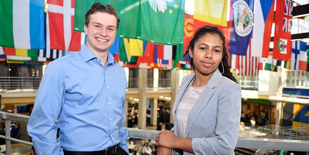 Two people standing in front of international flags hanging from the ceiling