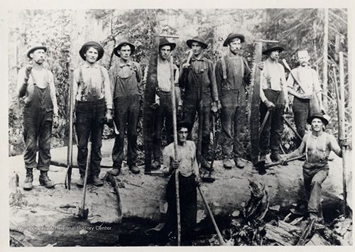 Group of men standing on a log in work clothes with tools